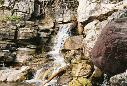 [The water seems to come out of the rock at the top of this image and goes back and forth acros the rock before dropping into a small pool. The are huge amounts of fragmented exposed rock in this image.]